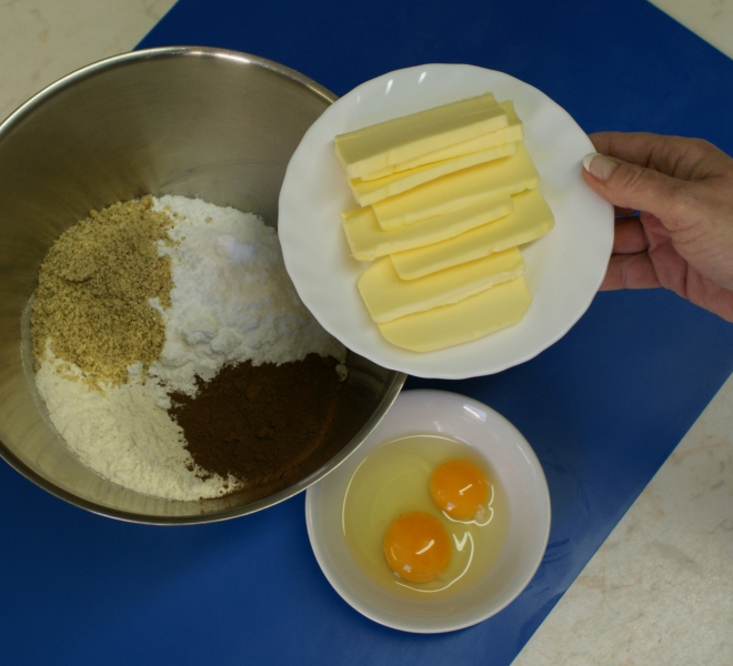 1. Mouku smíchejte s moučkovým cukrem, kakaem a mletými ořechy, přidejte nakrájené máslo, vejce s jedním žloutkem a v robotu vypracujte v jediném kroku na hladké těsto